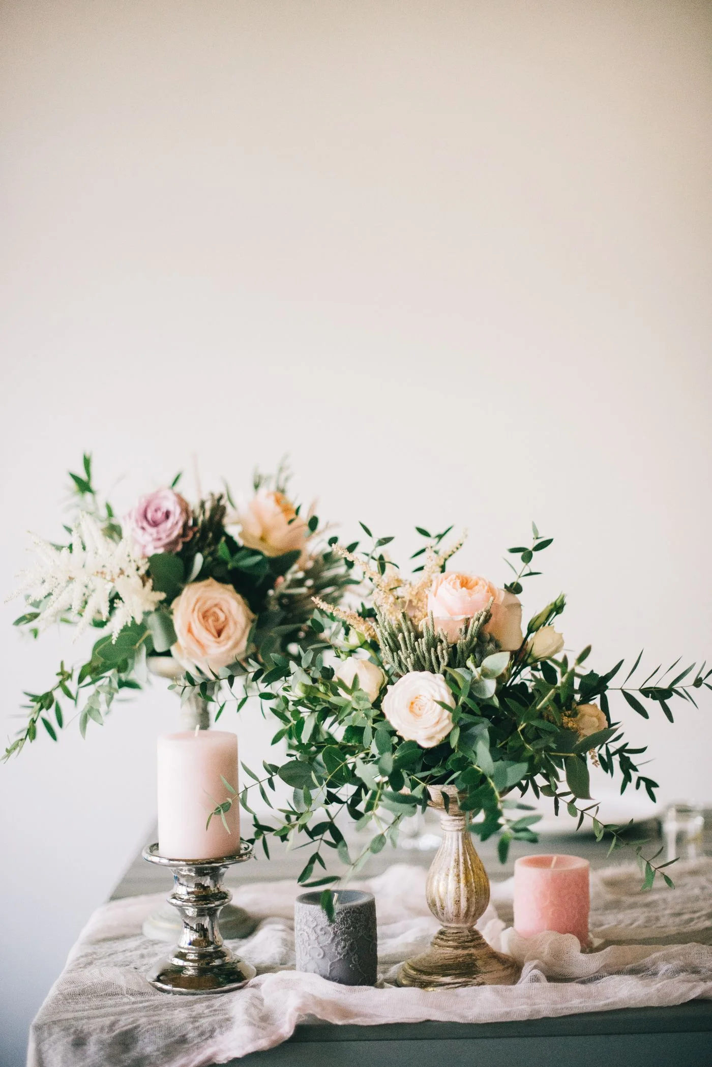 Rosas color durazno, follaje y velas rosas sobre una mesa de celebración.