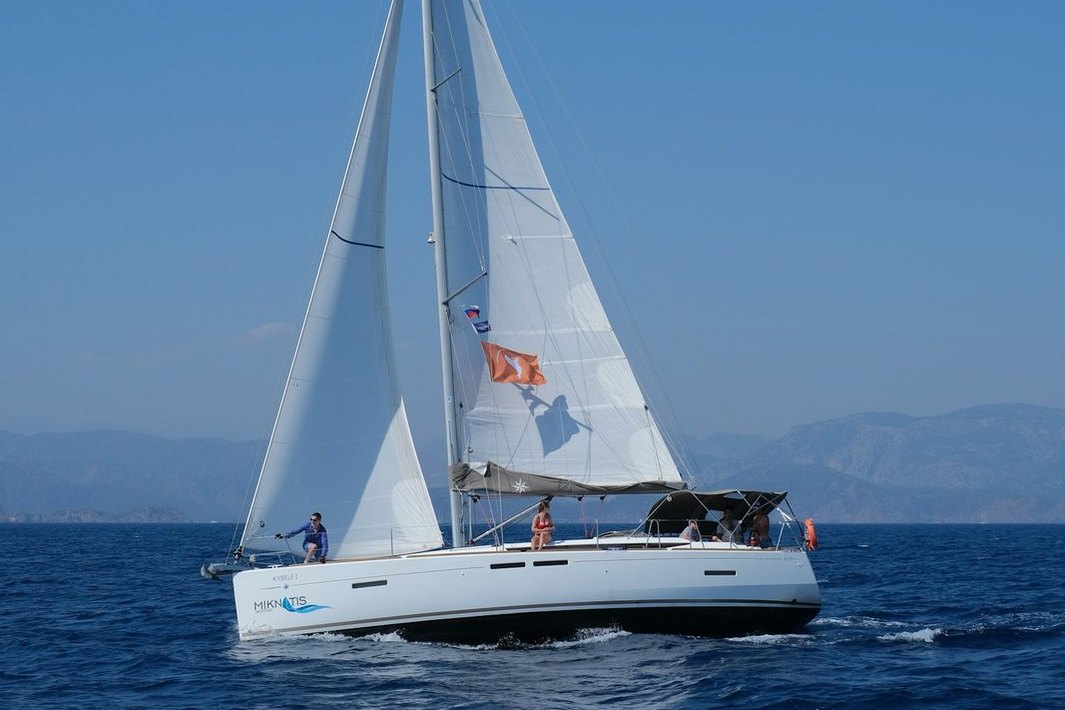 Personas a bordo de un velero con el mar y las montañas al fondo.