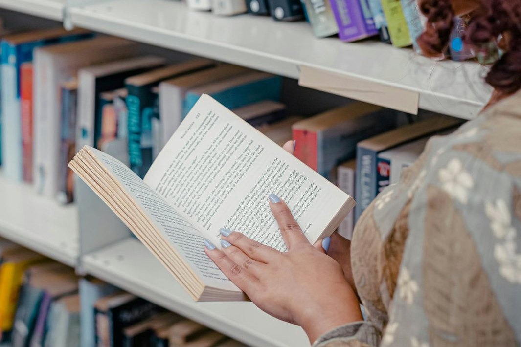 Una persona lee un libro junto a estantes llenos de libros.