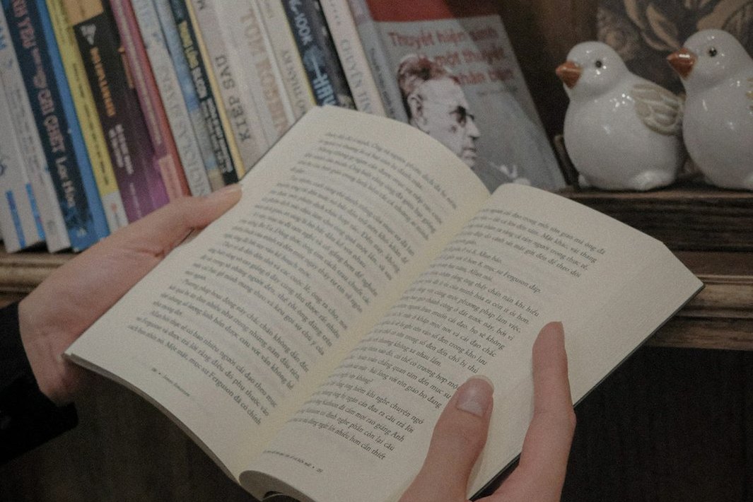 Una persona sostiene un libro abierto frente a una estantería.