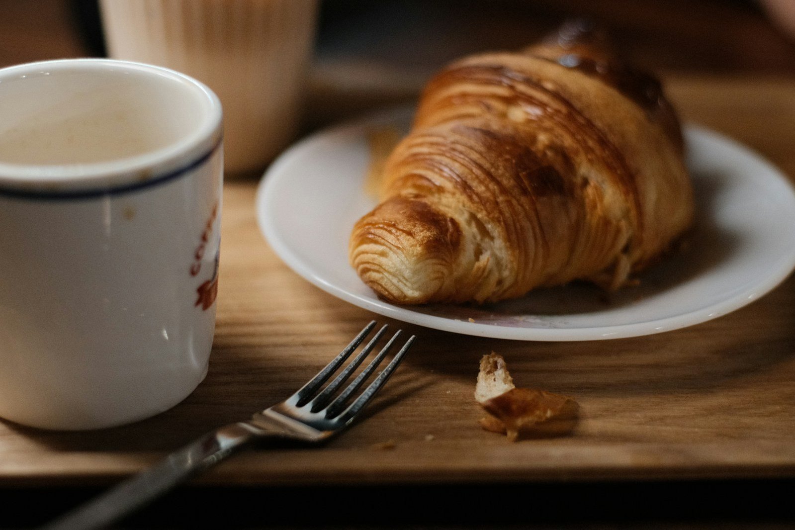 Un croissant y una taza de café sobre una mesa de madera.