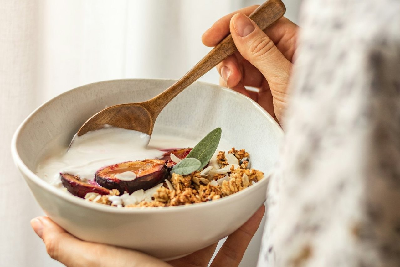 Un cuenco de desayuno con cereales y ciruelas sostenido entre las manos.