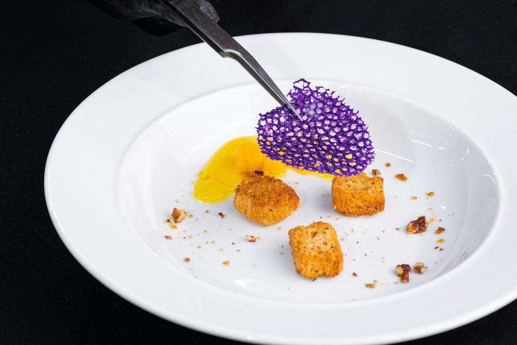 Manos con pinzas terminan de decorar un plato de cocina.