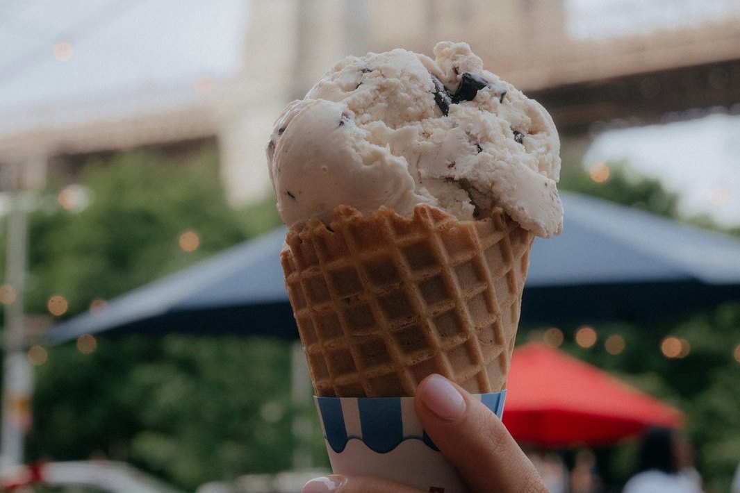 Una mano sostiene un cono de helado frente a un puente.