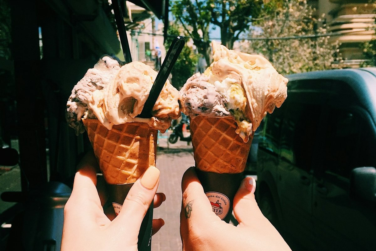Dos manos sostienen dos conos de helado durante un paseo.