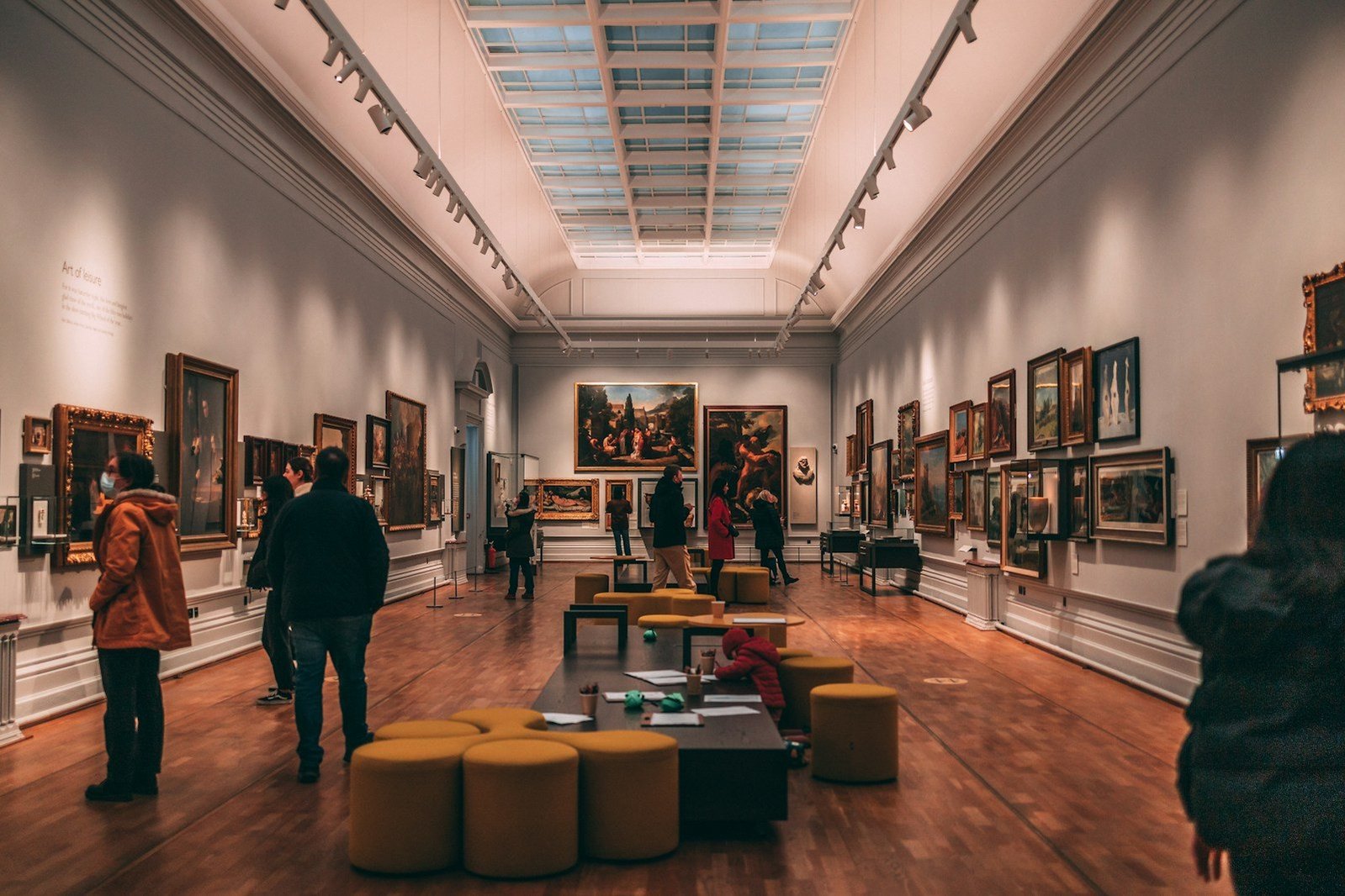 Visitantes recorren una galería de pintura iluminada por una claraboya.