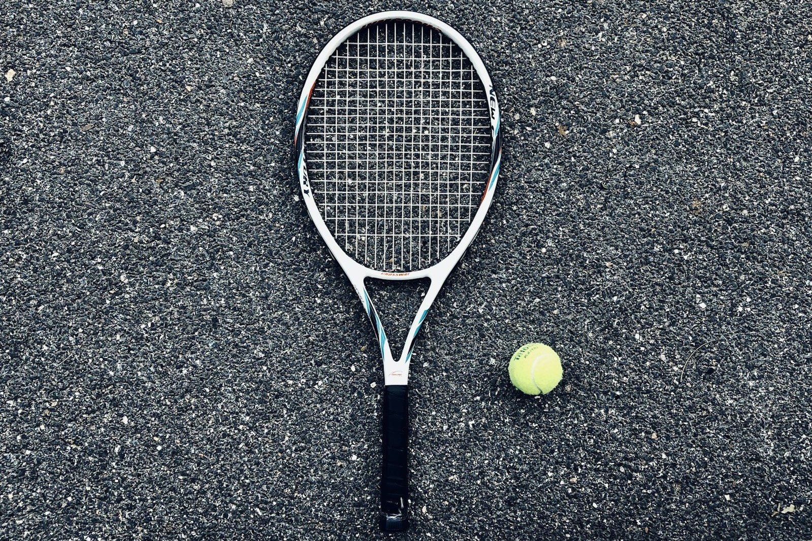 Una raqueta y una pelota de tenis sobre el suelo de una pista.