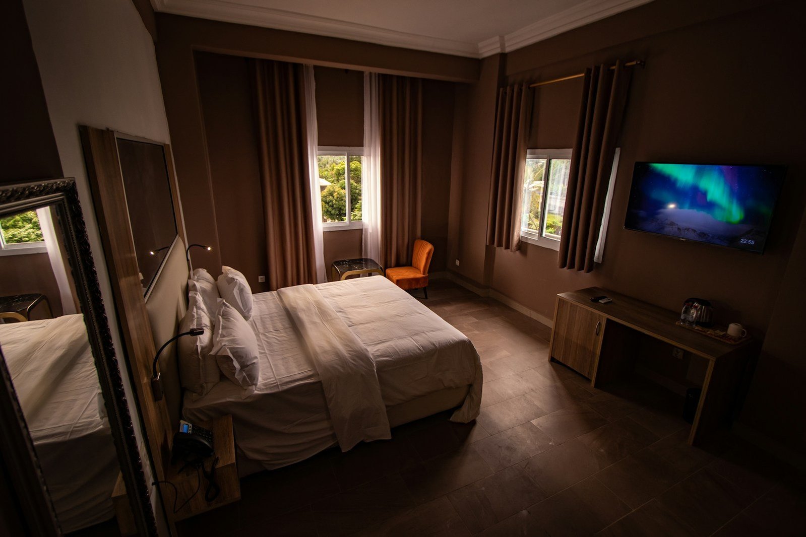 Habitación cálida de hotel con cama, ventanales y televisor.