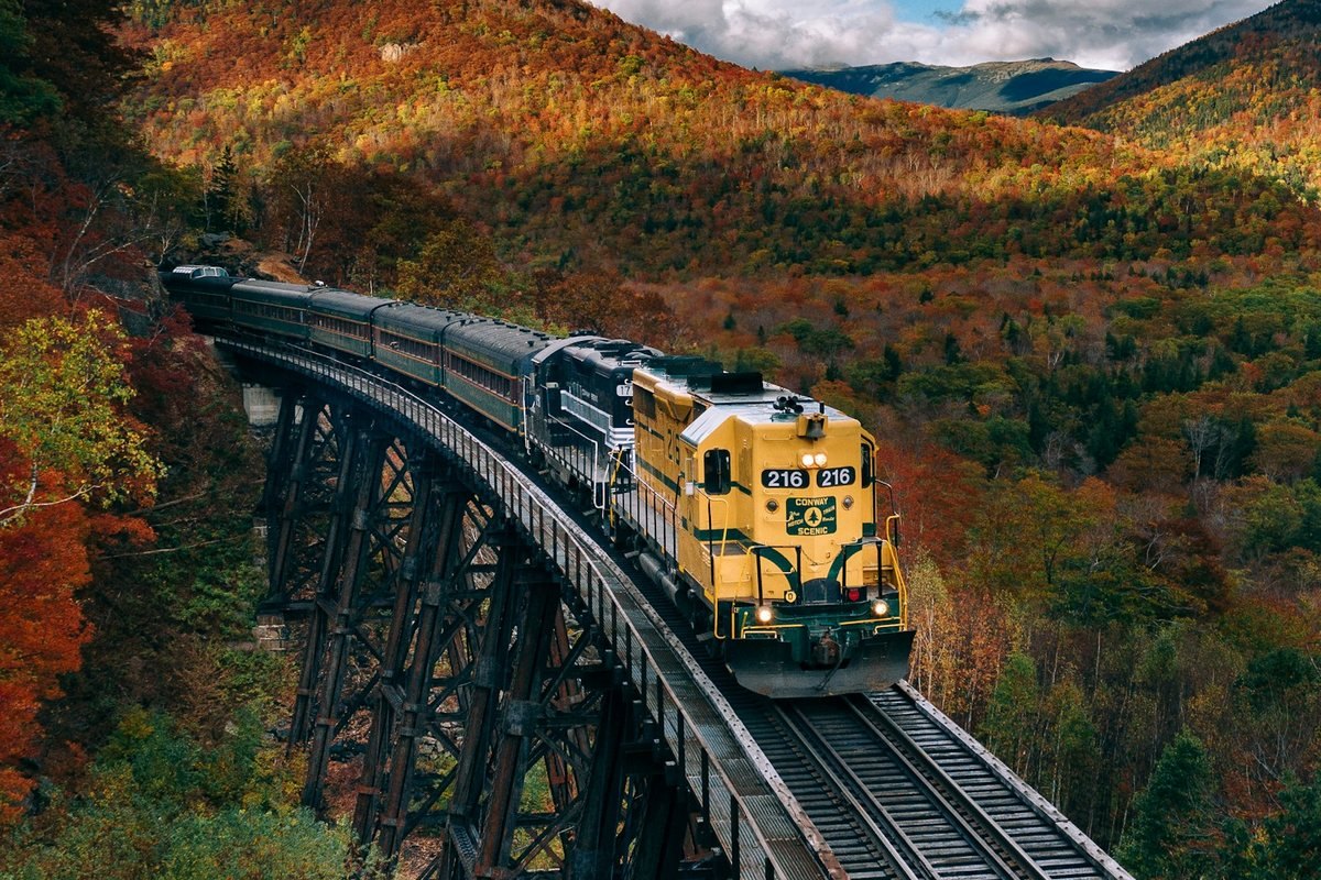 Un tren cruza un puente entre árboles de colores otoñales.